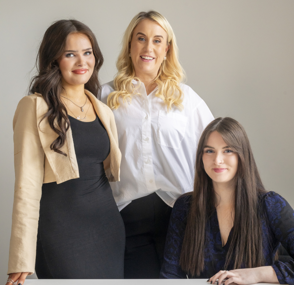 Three Call agents wearing white, black and cream stand in front of grey wall.