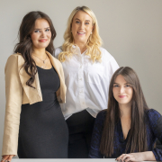 Three Call agents wearing white, black and cream stand in front of grey wall.