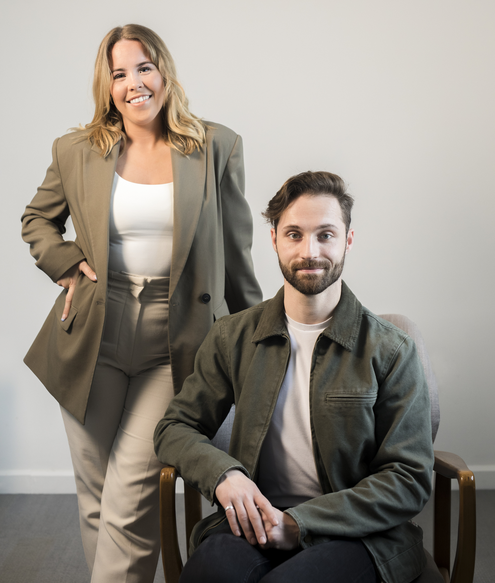 A call agent standing behind a sitting call agent. They are wearing green outfits with a white wall behind them.