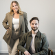 A call agent standing behind a sitting call agent. They are wearing green outfits with a white wall behind them.