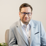 Man wearing white shirt and blue blazer sat infront of grey wall.