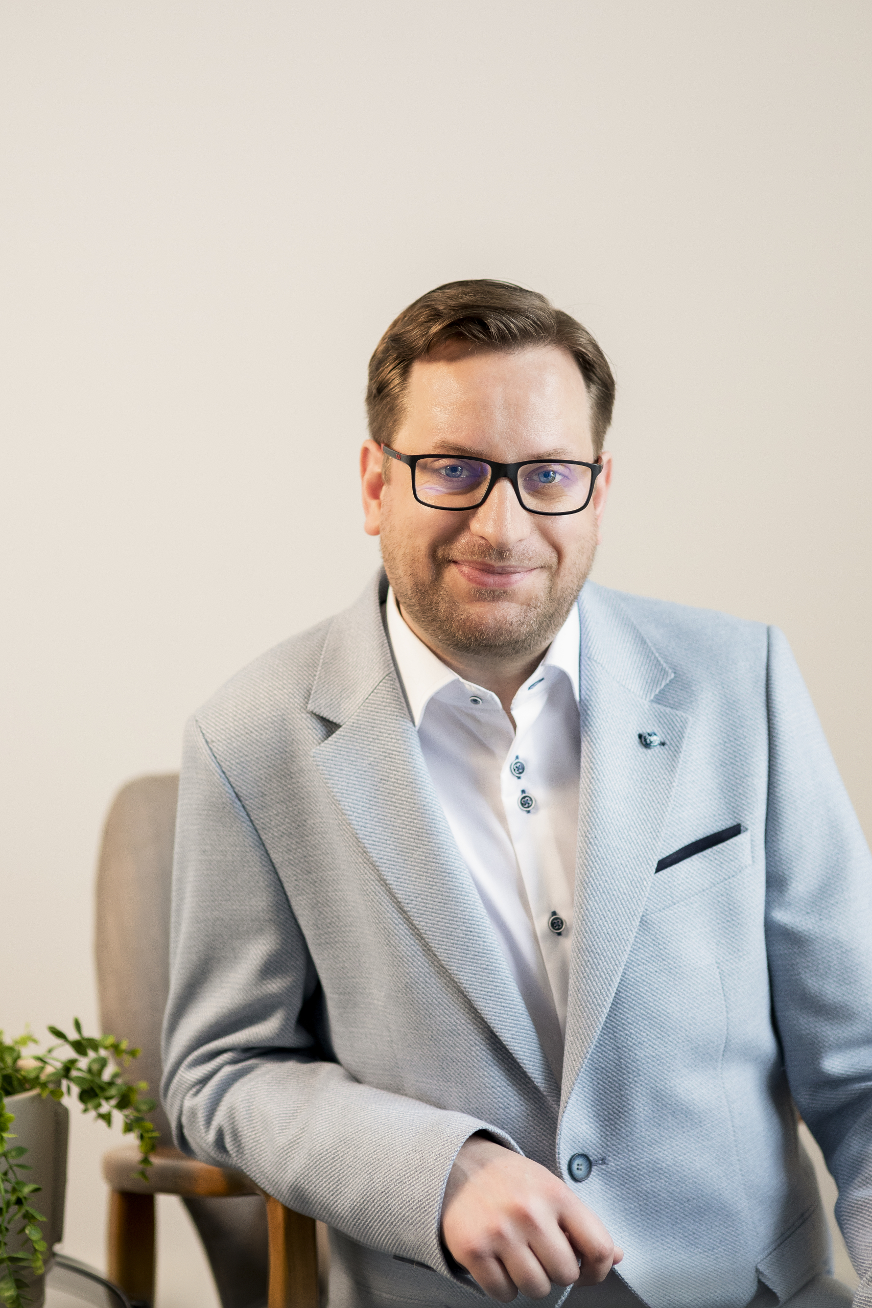 Man wearing white shirt and blue blazer sat infront of grey wall.